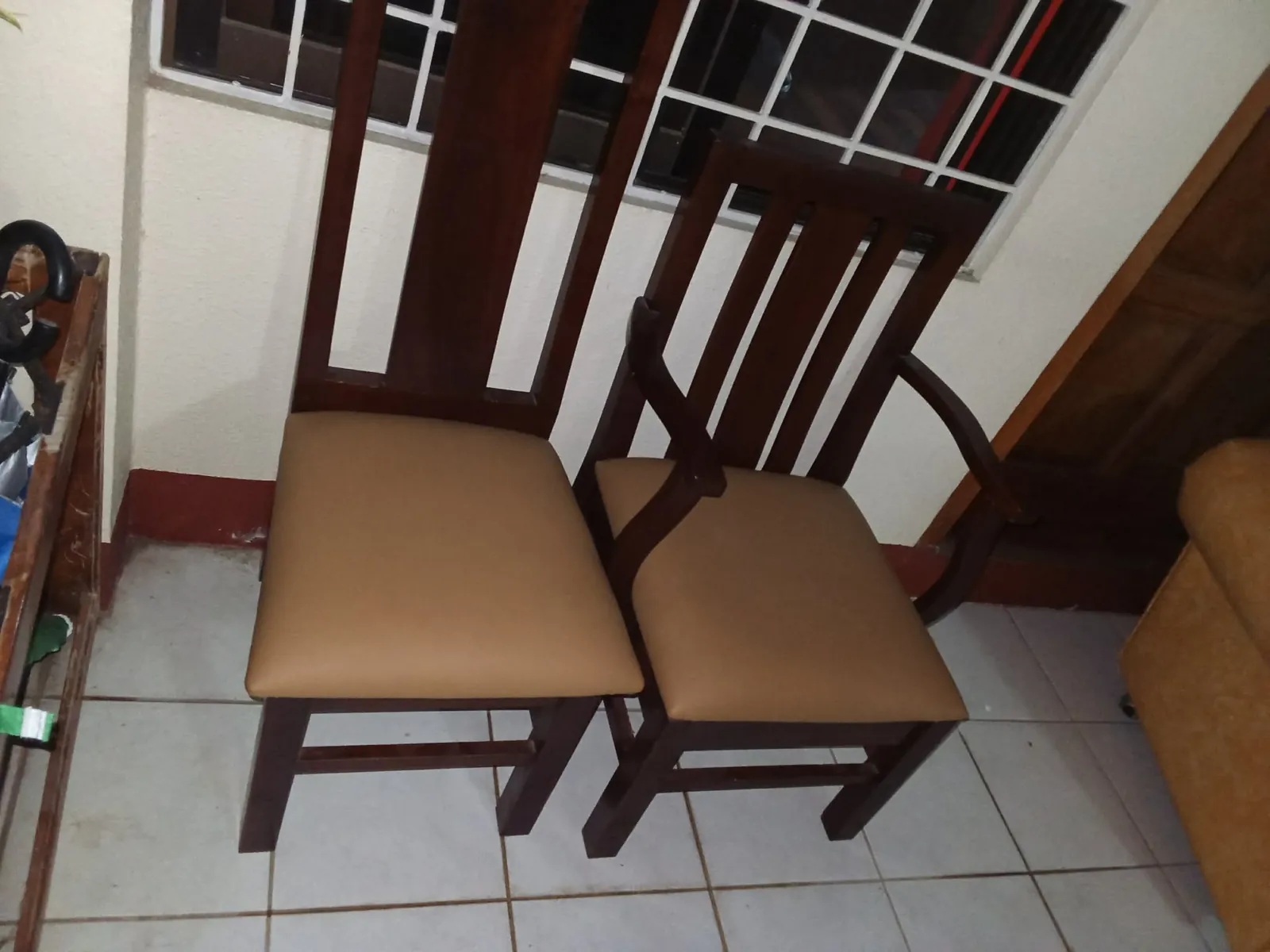 Two dark wooden dining chairs with tan upholstered seats and tall slatted backrests