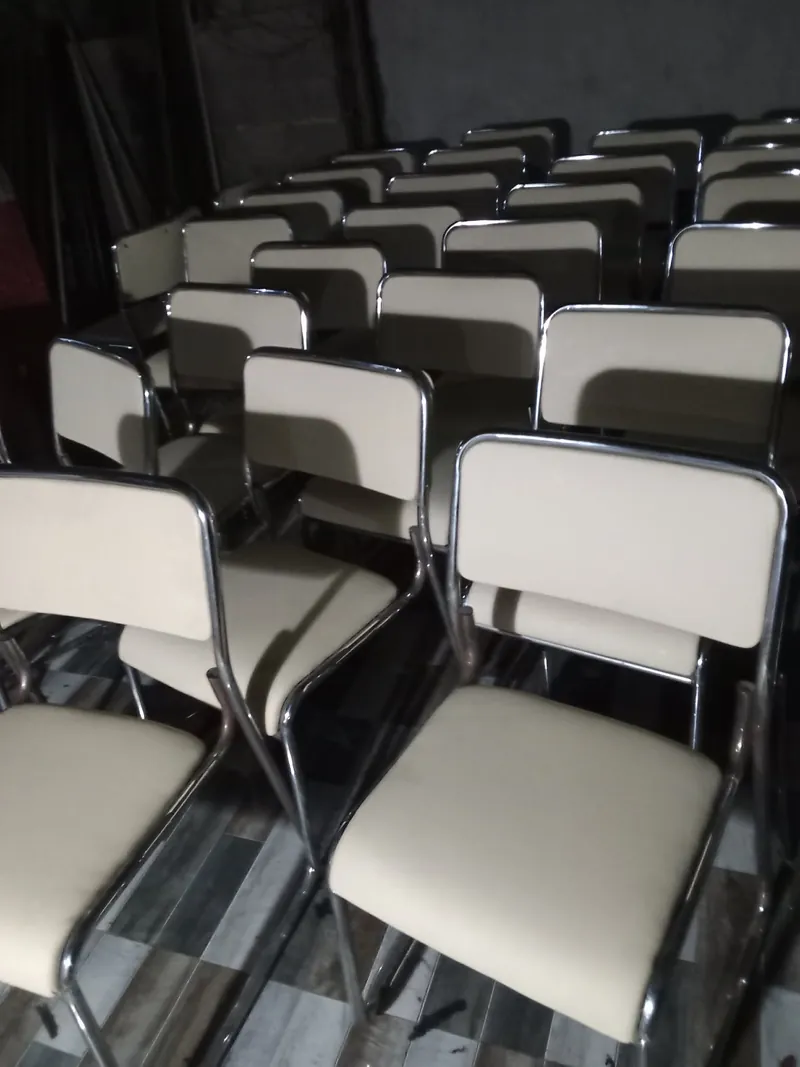 Black vinyl stacking chair seen from the side, its chrome sled base running unbroken from front leg to floor