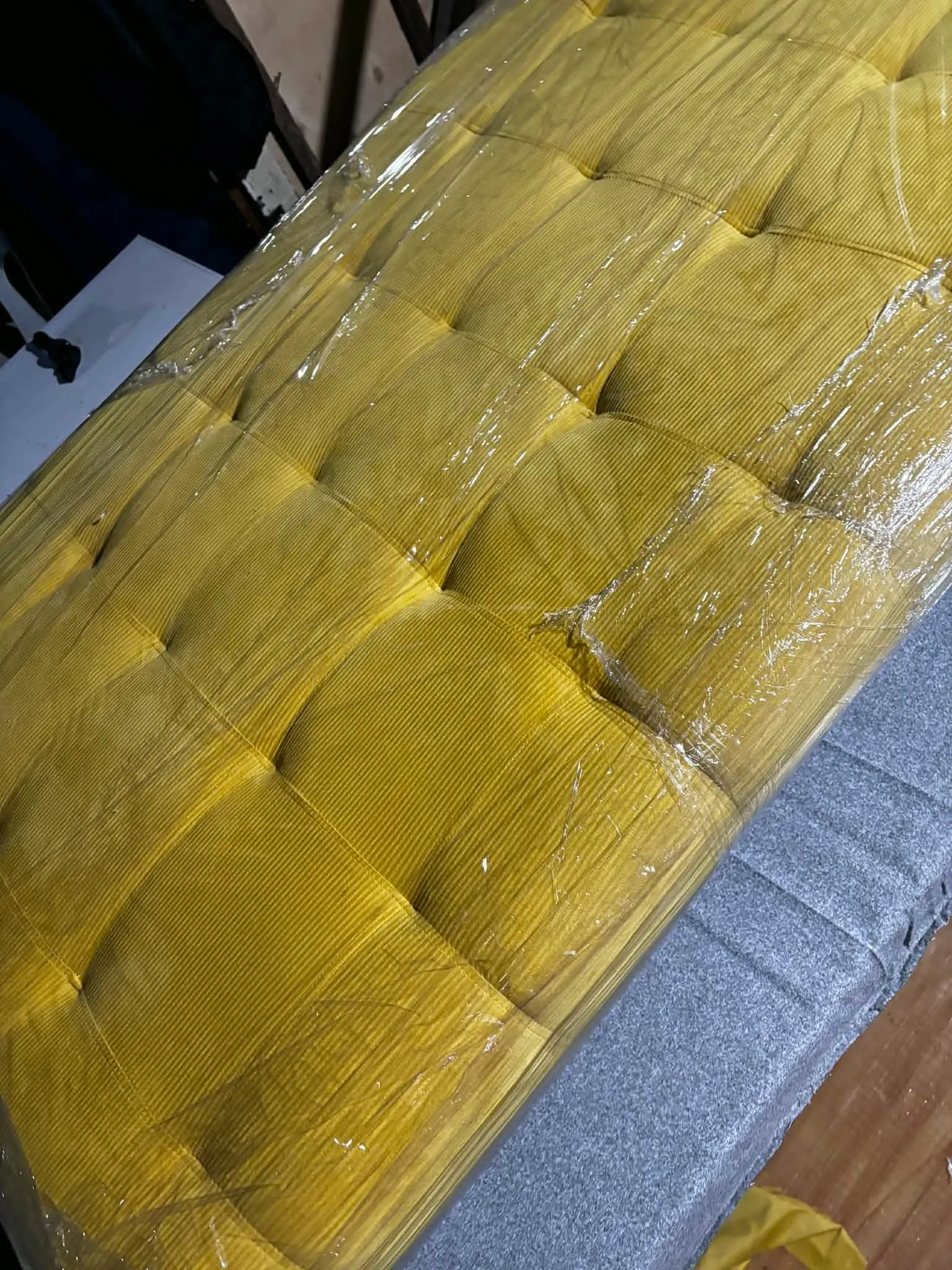 Mustard corduroy sofa bed seen from above, tufted into a stitched grid of squares, wrapped in plastic